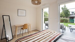 A bedroom with a bed, a desk, a chair, a large mirror, and a view of the outdoors through a sliding door. - Seaside house, all comforts - close to the beaches (Dinard)