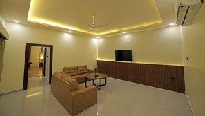 A modern living room with a sectional sofa, a coffee table, recessed ceiling lighting, a ceiling fan, and a mounted TV. - Lake Valley Resort and Spa, Tirupati  (Chinnagottigallu)