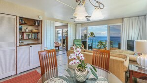 A spacious living area with a dining table, chairs, a sofa, and a balcony with a view of the ocean.