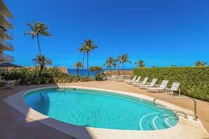 A pool with clear blue water, surrounded by lounge chairs and palm trees, with a view of the ocean.