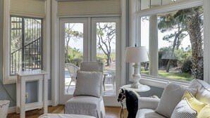 Ein Zimmer mit Blick auf den Strand, ein gestreifter Ohrensessel, eine Couch mit Kissen und ein Tisch mit einer Lampe.