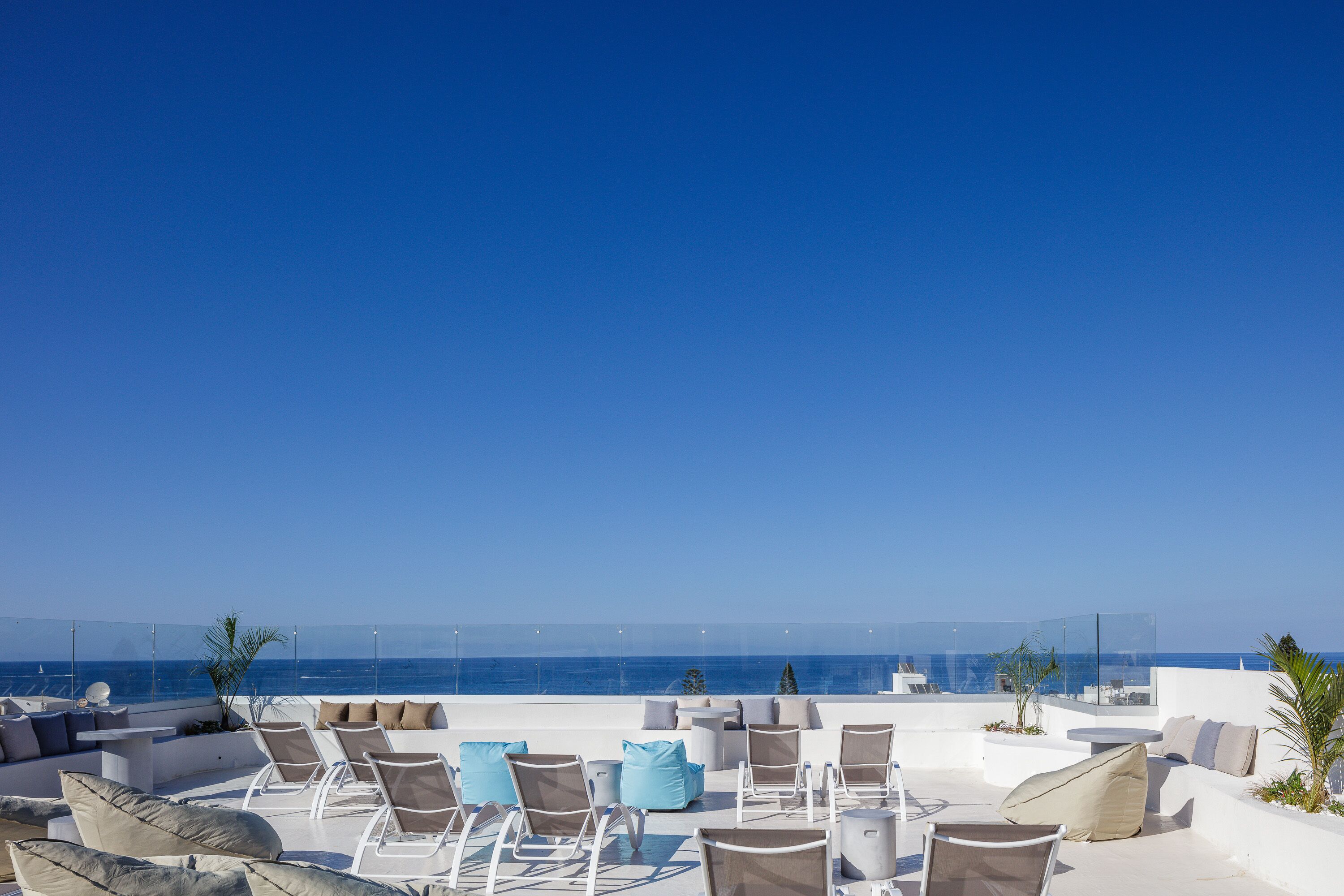 A rooftop terrace with white furniture and a clear view of the sea.