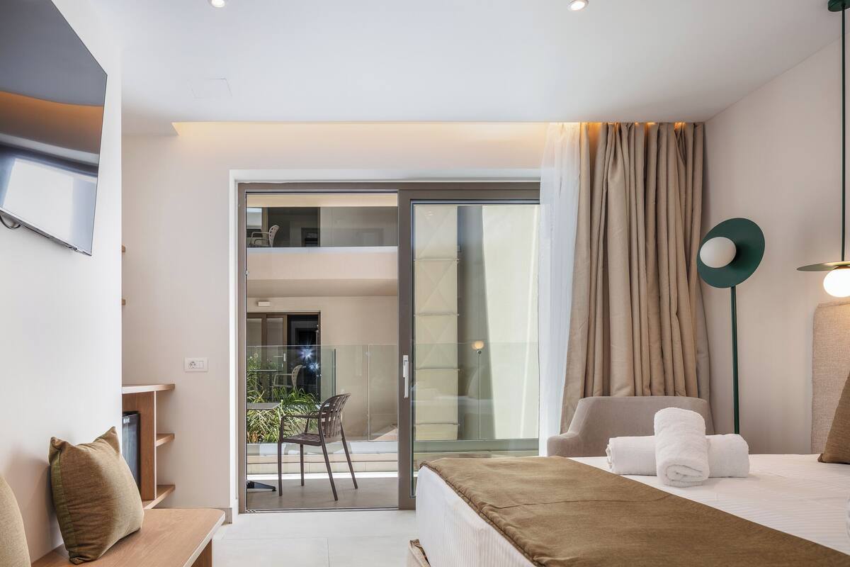 A modern hotel room with a bed, a seating area, and a balcony with a glass door.