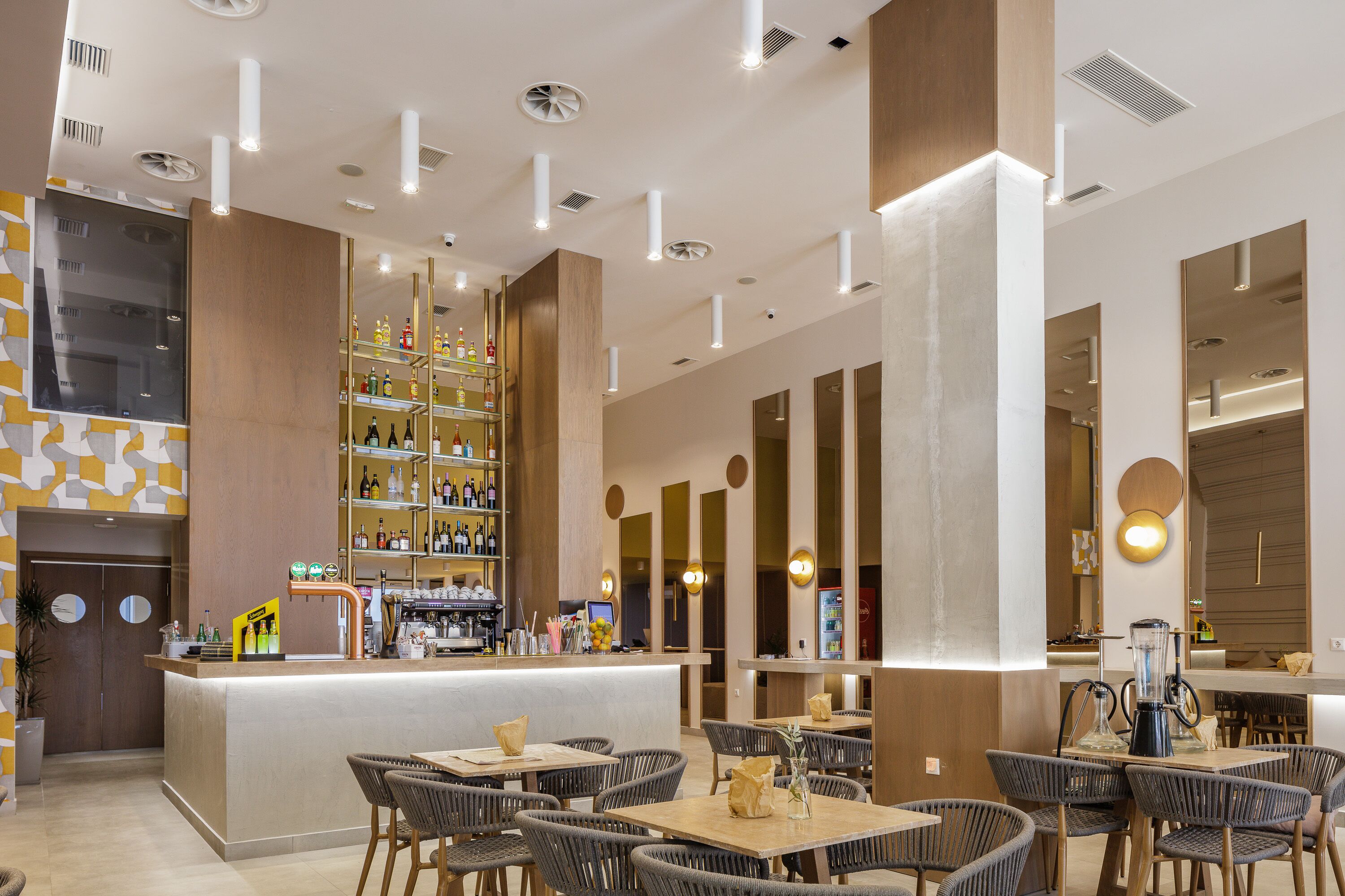 Una zona de bar moderna con una barra, estantes llenos de botellas y asientos con mesas y sillas.