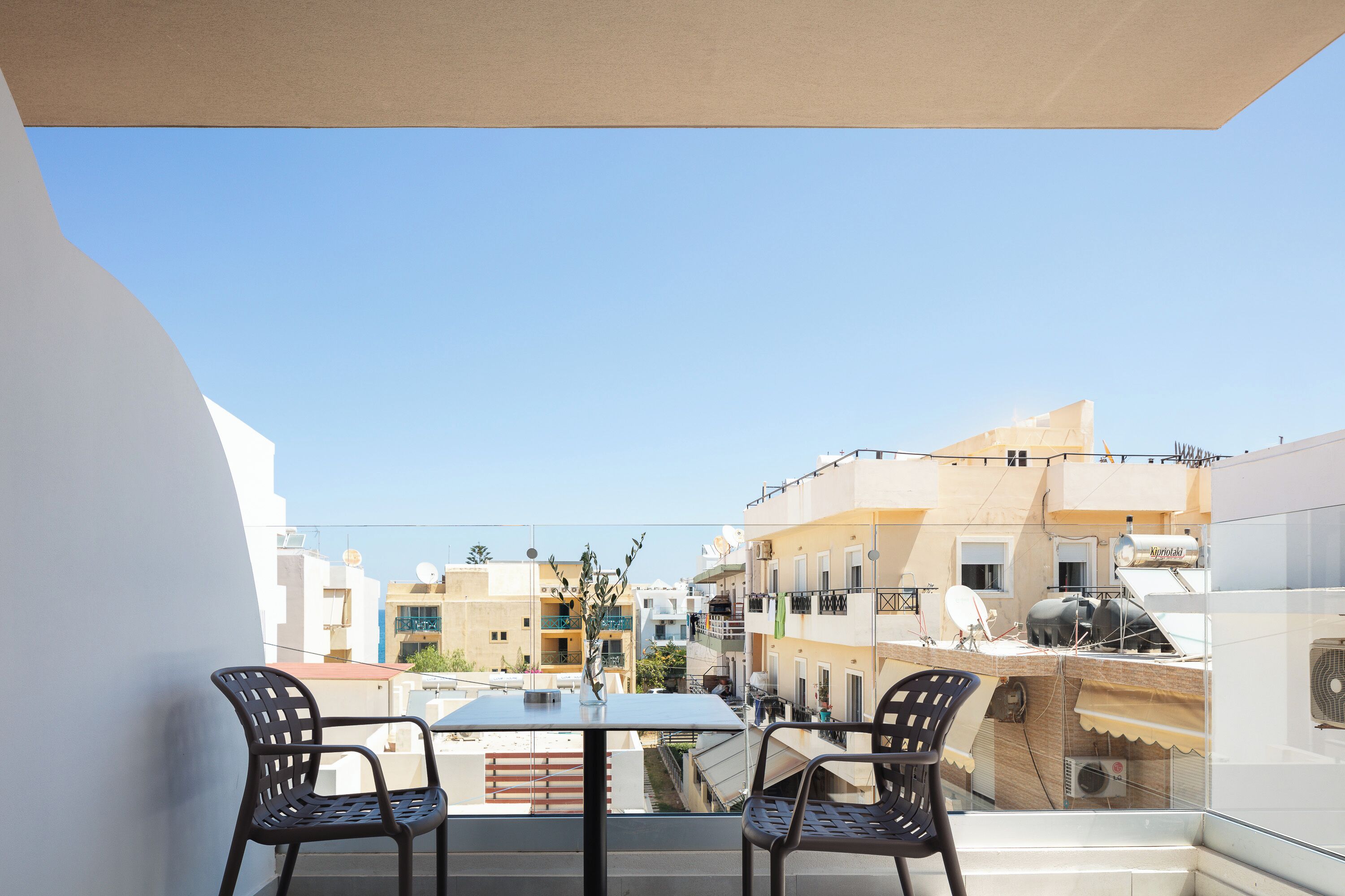 A balcony with two chairs and a table, overlooking a residential area with buildings and a clear sky.