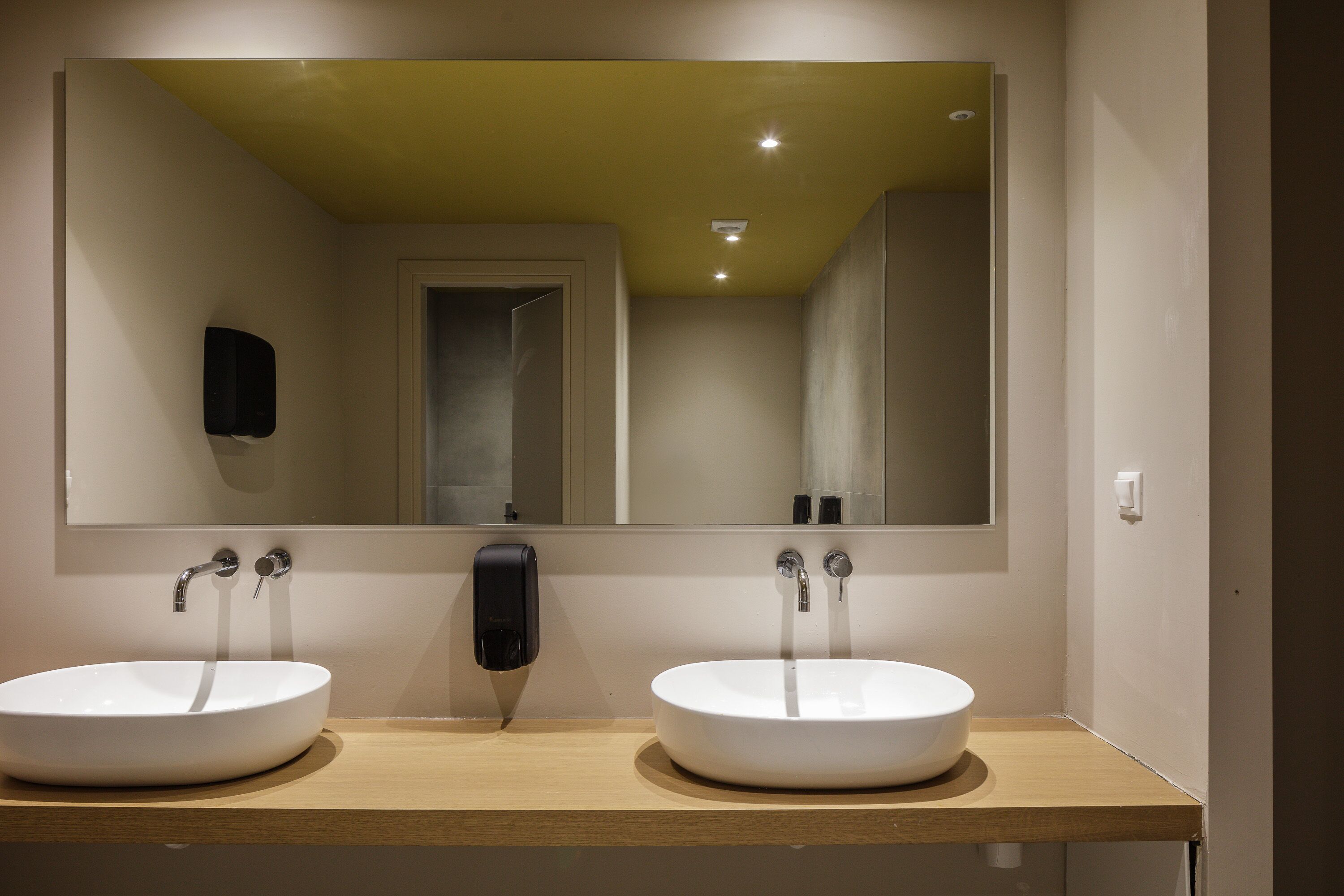 Een badkamer met twee wasbakken, een grote spiegel en een zeepdispenser.