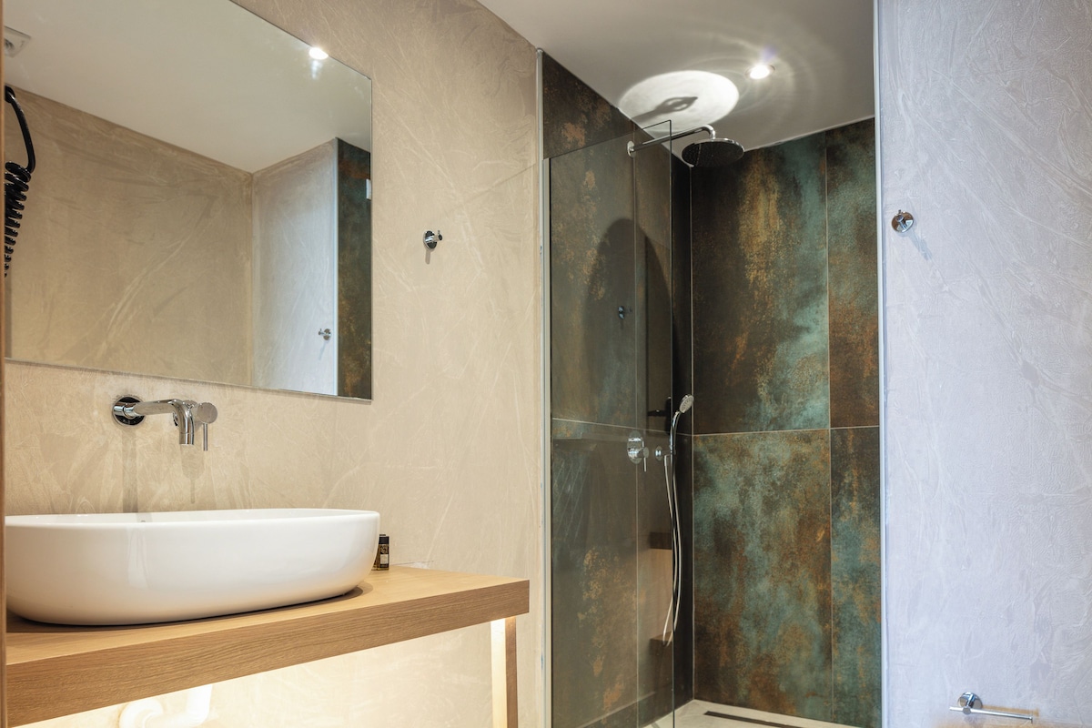 Un baño moderno con un espejo grande, un lavabo tipo recipiente y una zona de ducha con paredes de vidrio.