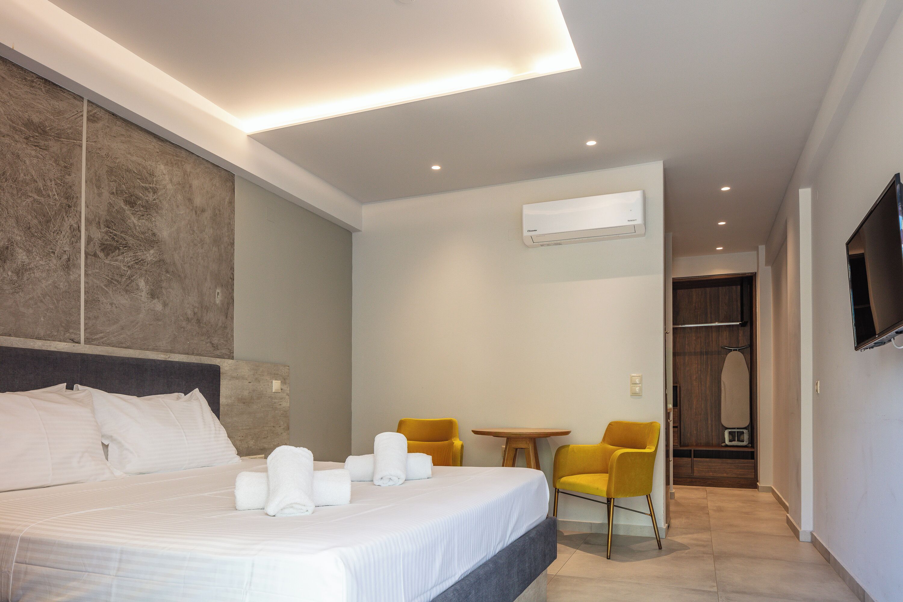Ein modernes Hotelzimmer mit einem großen Bett, einem kleinen Tisch, zwei Stühlen und einem an der Wand befestigten Fernseher.