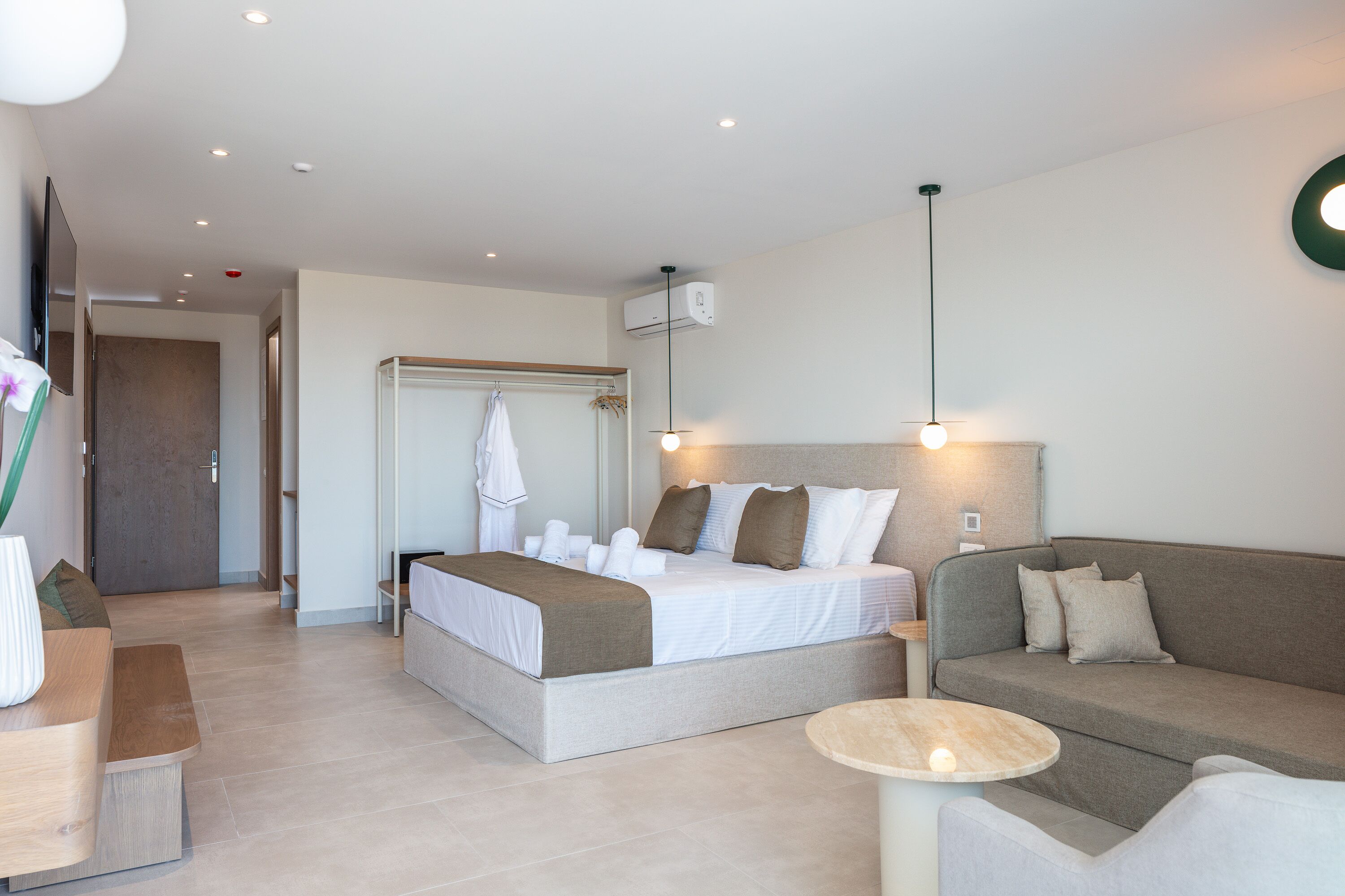 A modern hotel room with a bed, a sofa, a small table, and a TV.