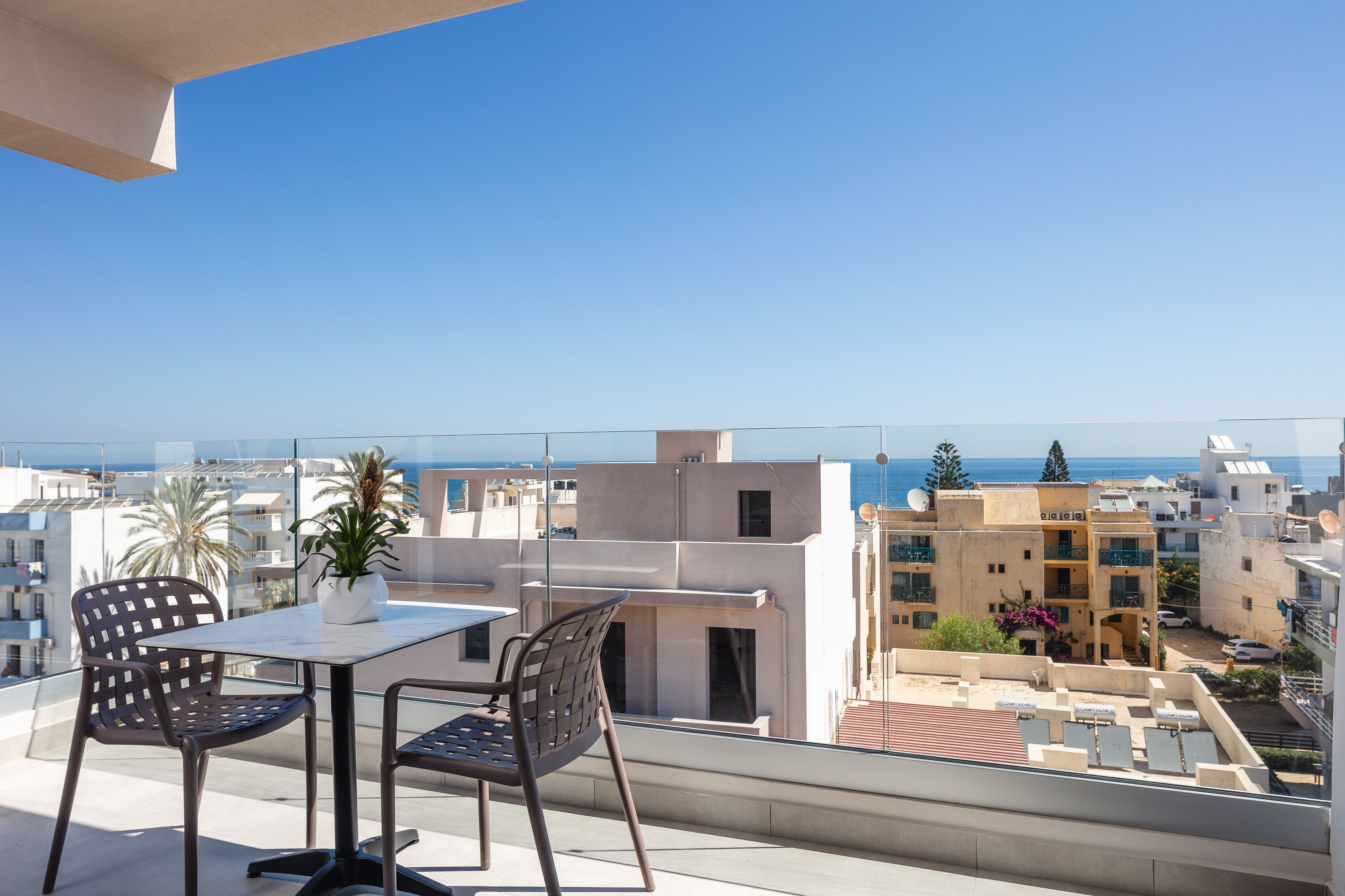 A balcony with a table and chairs, overlooking a cityscape and the sea.