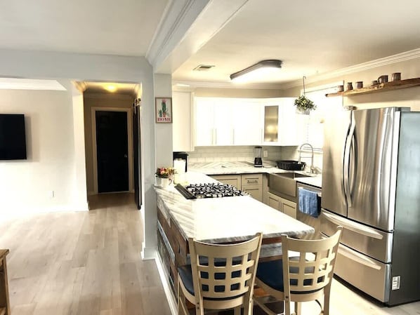A modern kitchen with a central island, stainless steel appliances, and a dining area with two chairs. - A Poolside Paradise (Pensacola)