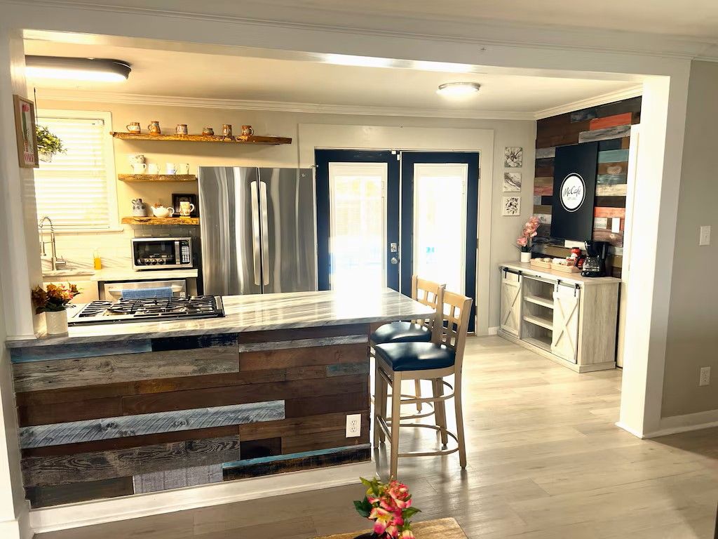 A modern kitchen with a central island, wooden shelves, and a dining area with a bar stool.