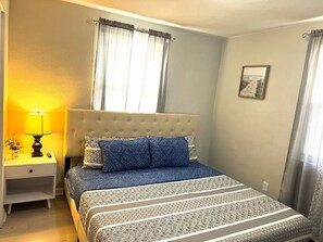 A bedroom with a bed, a nightstand, a lamp, and a window with curtains.