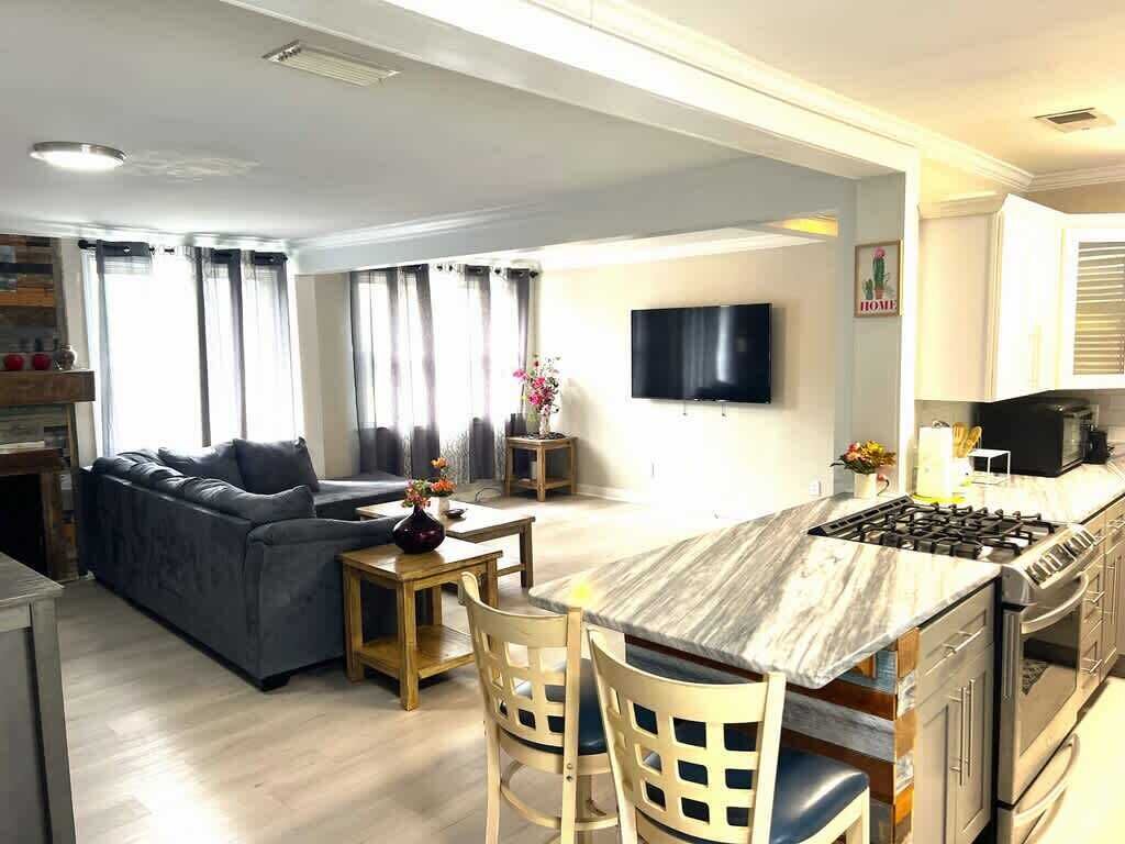 Una cocina moderna con una isla central, una zona de comedor con un sofá y un televisor de pantalla plana en la pared.
