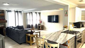 Una cocina moderna con una isla central, una zona de comedor con un sofá y un televisor de pantalla plana en la pared.