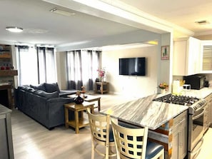 A modern kitchen with a central island, a dining area with a sofa, and a flat-screen TV mounted on the wall. - A Poolside Paradise (Pensacola)