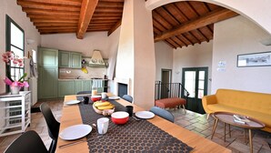 Un vaste espace de salle à manger avec une table en bois dressée pour un repas, un canapé jaune et une cuisine en arrière-plan.