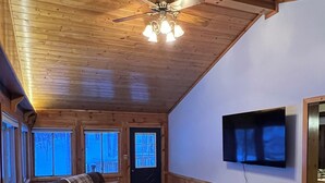 Una sala de estar acogedora con un sofá seccional, techo de madera, televisor de pantalla plana en la pared y ventilador de techo.