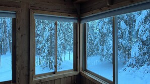 Una cabaña con paredes de madera y ventanas amplias que dan a un bosque nevado.