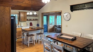 Una cocina con armarios de madera, una isla central con taburetes, un ventilador de techo y un reloj en la pared.
