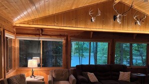 Un interior de cabaña acogedor con paredes de madera, un ventanal con vistas a un bosque y una chimenea.