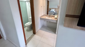 Casa de banho com sanita, chuveiro e lavatório com espelho.