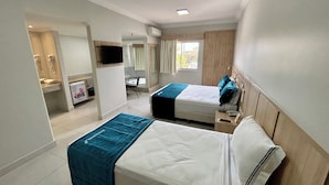 Quarto de hotel com duas camas, banheiro, uma pequena escrivaninha e janela.