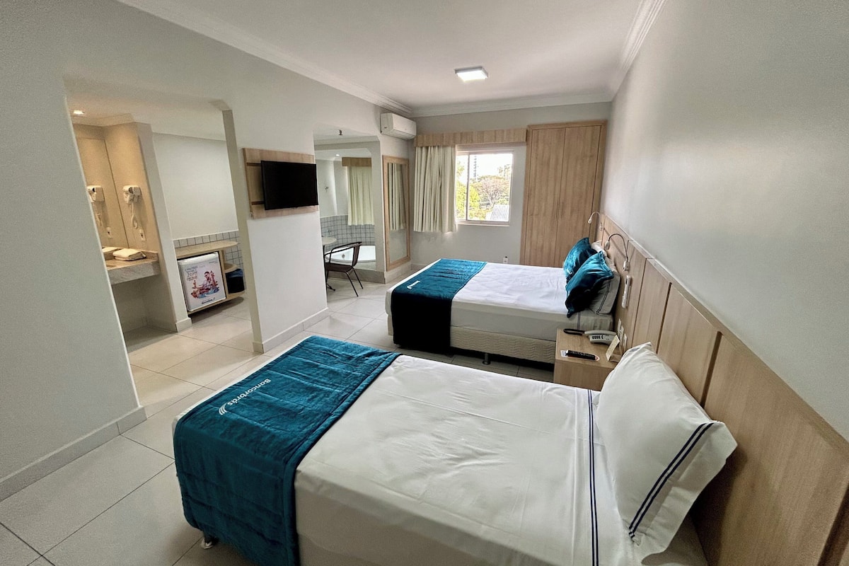 A hotel room with two beds, a bathroom, a small desk, and a window.
