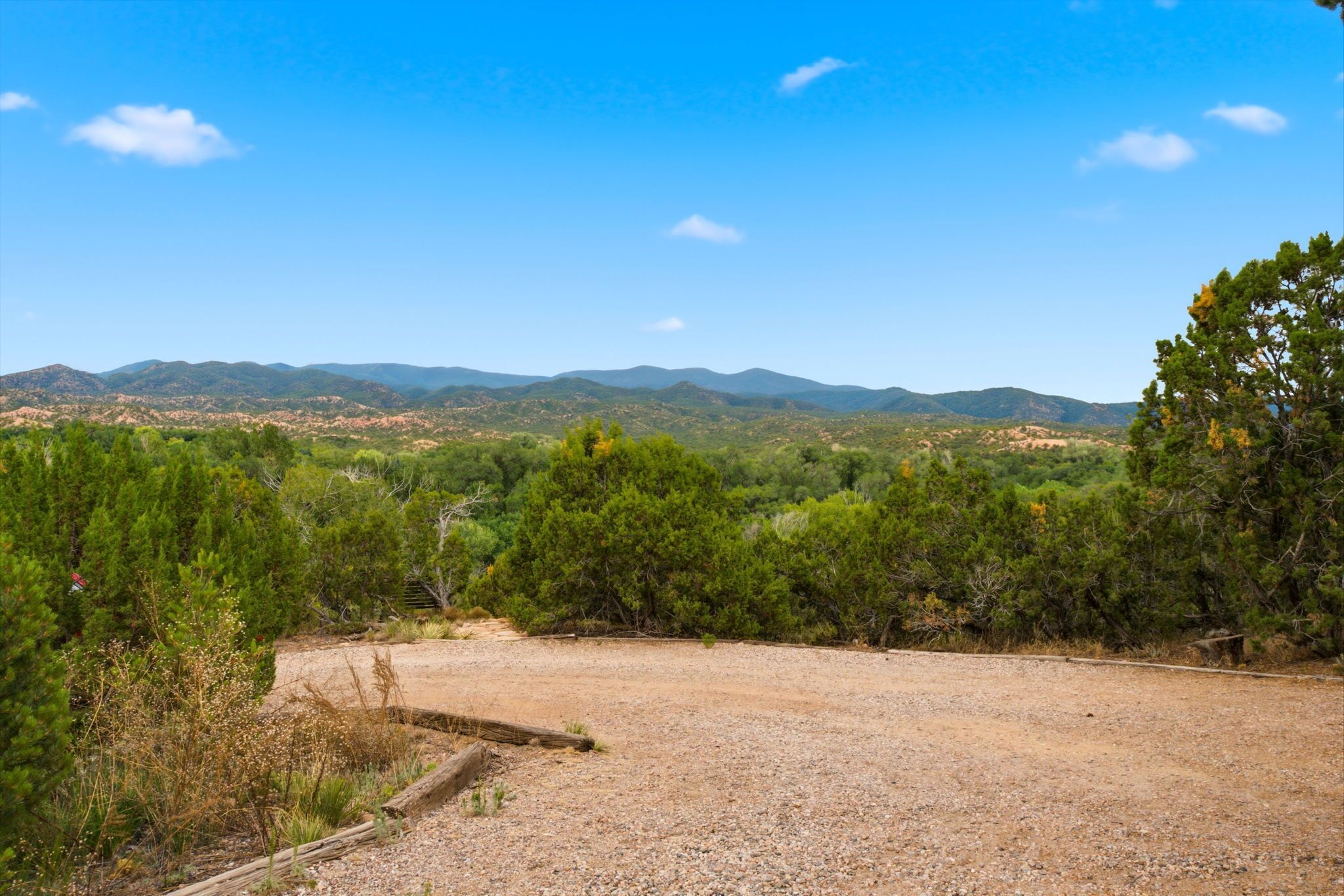 A gravel area with sparse vegetation and distant mountains under a clear sky.