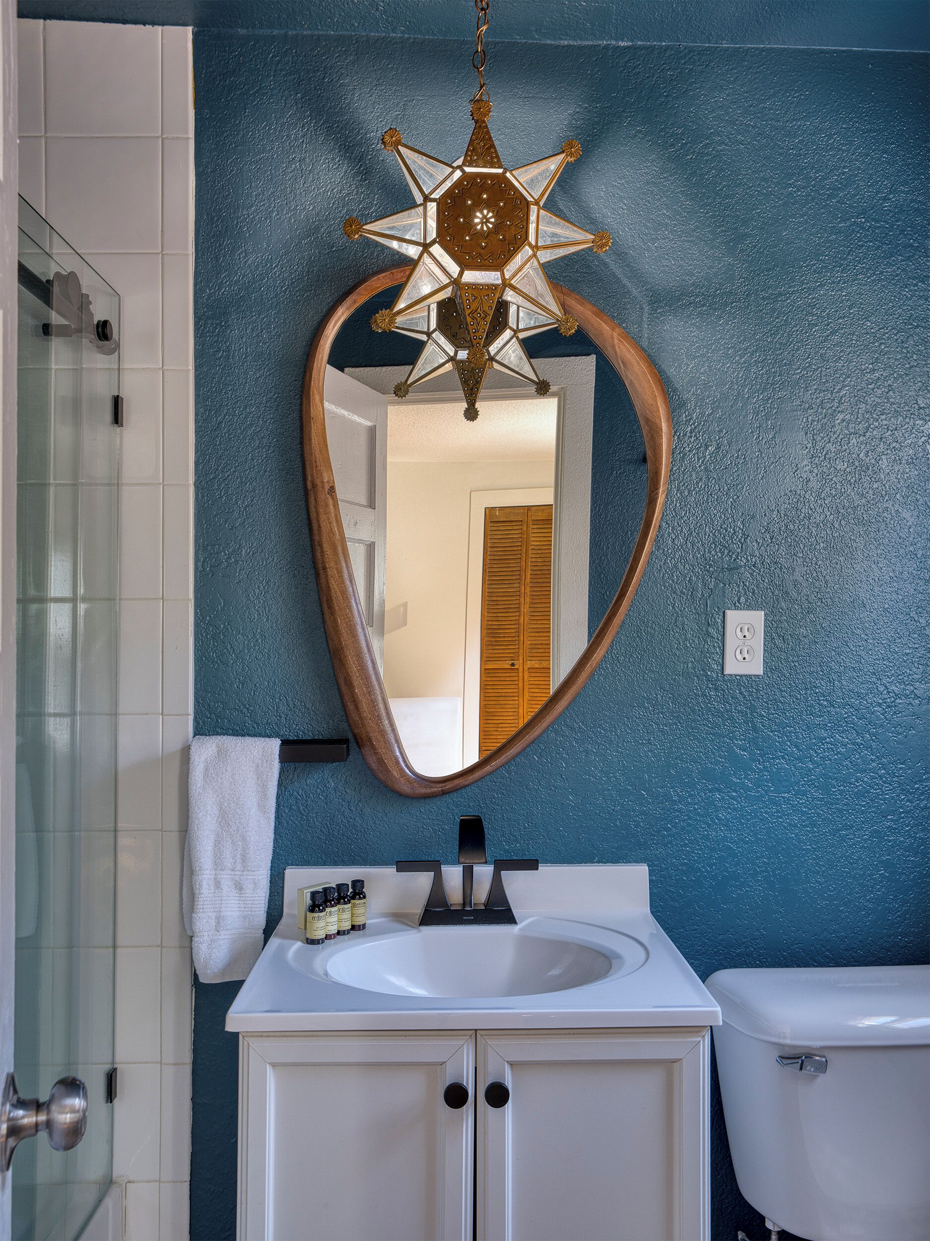 Un bagno con una lampada a sospensione a forma di stella, uno specchio con cornice ovale, un lavandino bianco e un water.