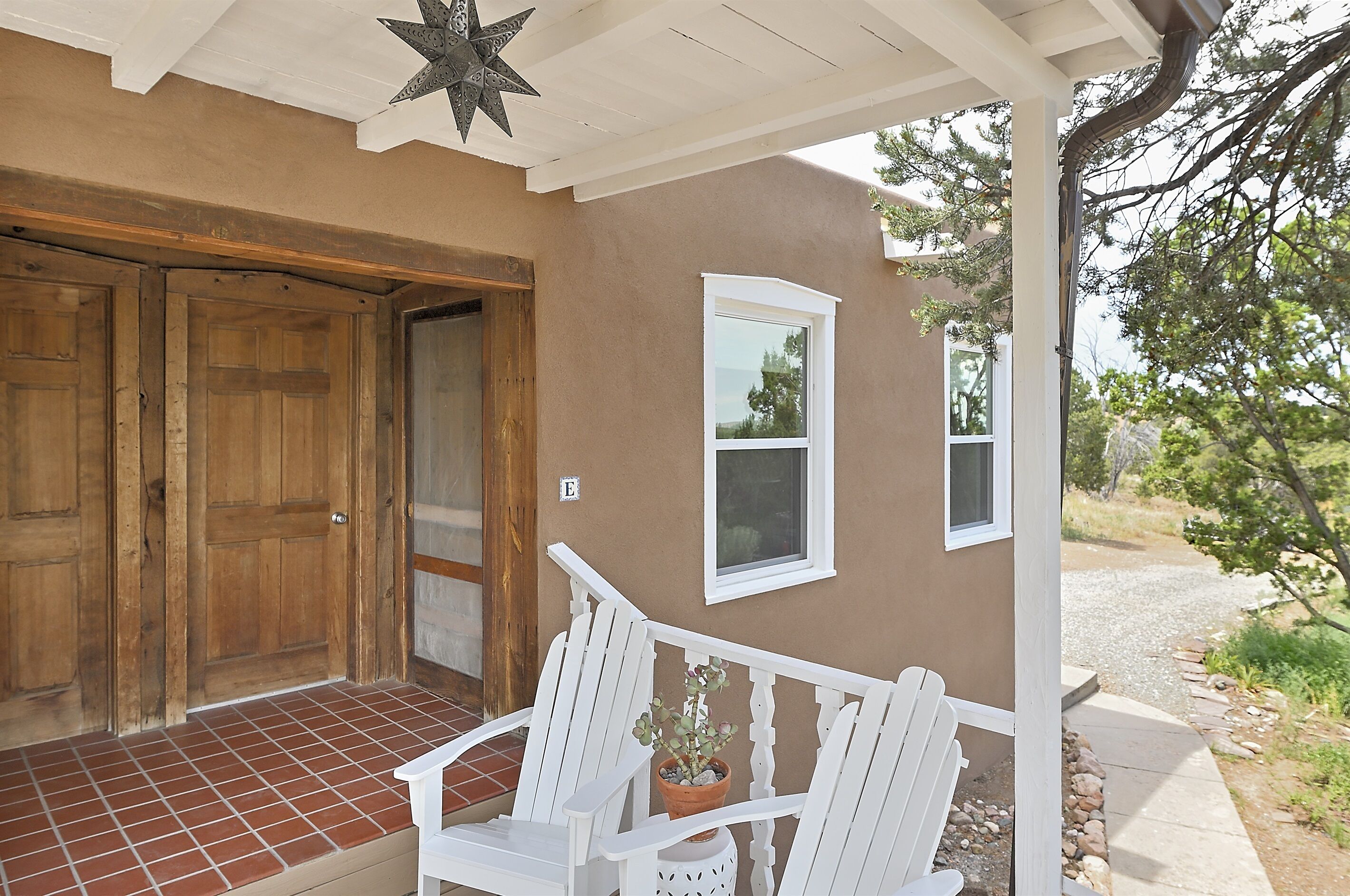 A porch with white wooden chairs, a potted plant, and a star decoration.