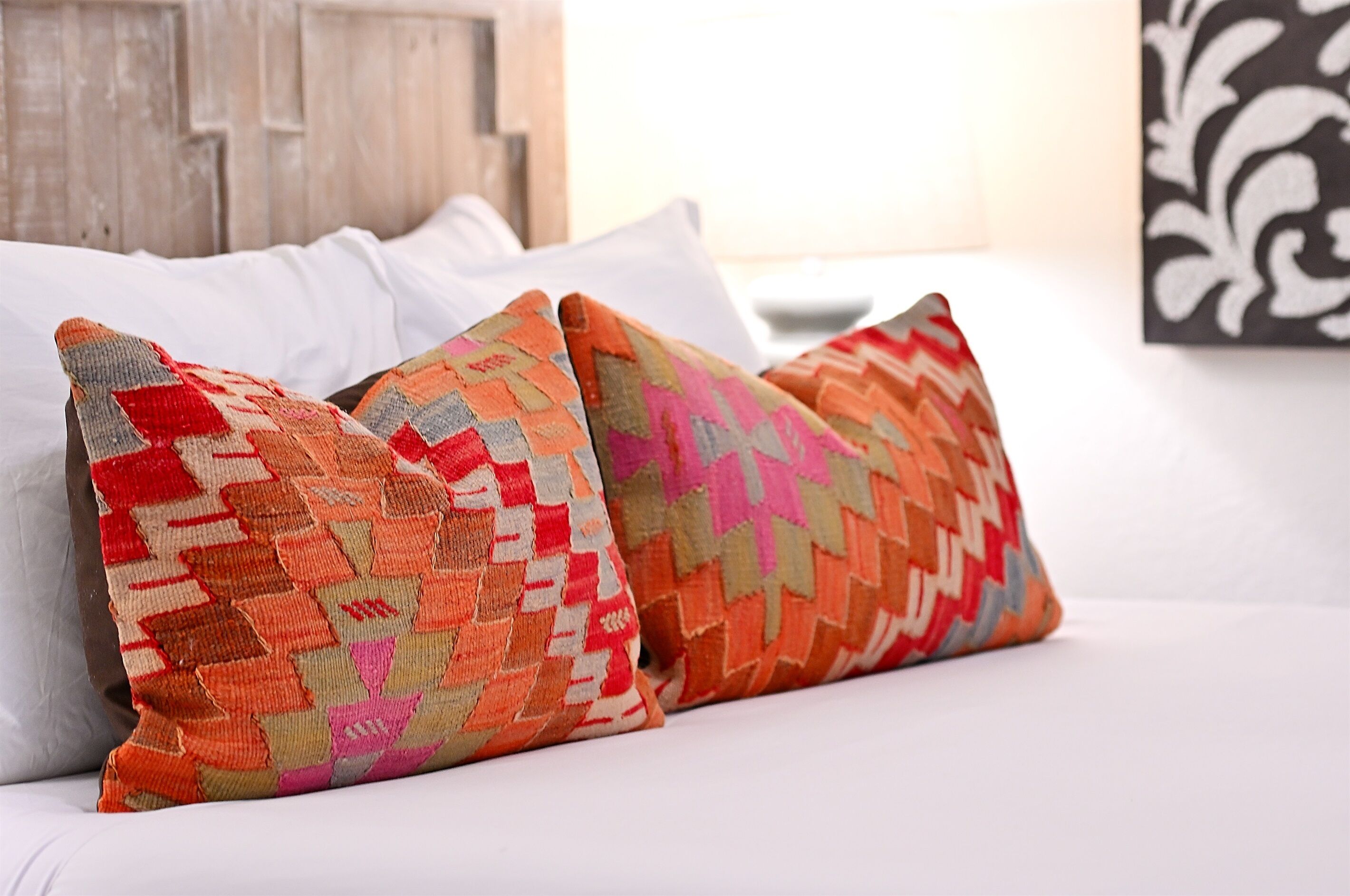 Un lit avec une literie blanche et deux coussins colorés à motifs.