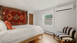 Une chambre à coucher avec un lit, une fenêtre, un appareil de climatisation et une chaise.