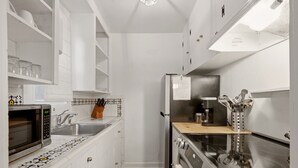Une cuisine de taille réduite, avec des meubles blancs, un four à micro-ondes, un évier, une cuisinière et un réfrigérateur.