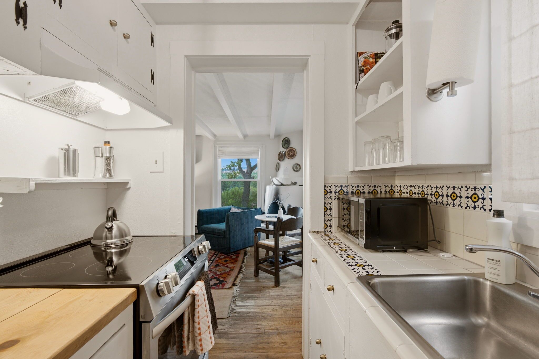 Cocina moderna con estufa, microondas y lavamanos. Hay una zona de comedor con mesa y sillas.
