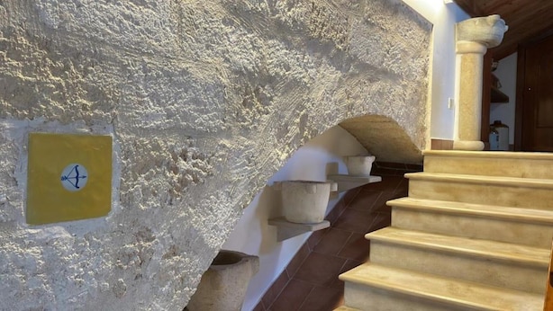 Un muro in pietra con un quadrato giallo e un simbolo, una scala in pietra e una porta in legno.