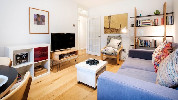Ett modernt vardagsrum med en platt-TV, en bokhylla, en bekväm soffa och en matplats.