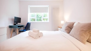 Ett hotellrum med en säng, ett skrivbord med en dator, en stol och ett fönster med gardiner.