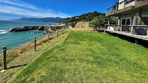 A coastal property with a grassy lawn, a wooden deck, and a view of the ocean and mountains.