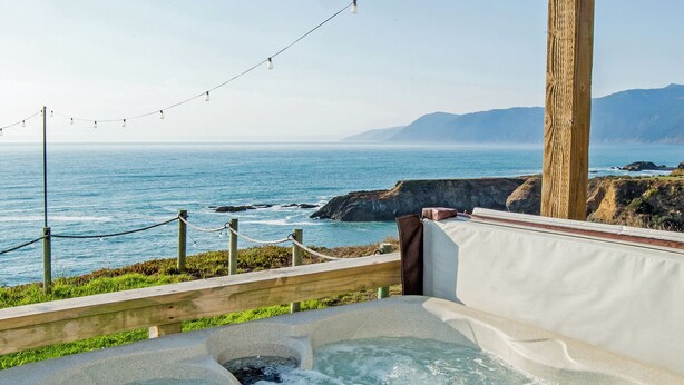 A hot tub with a view of the ocean, a wooden post, and a string of lights.