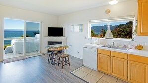 A modern kitchen with a large window, a dining area with a glass table, and a view of the ocean.