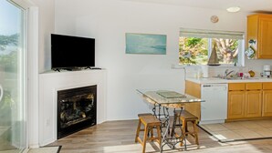 A modern kitchen with a flat-screen TV, a fireplace, wooden cabinets, and a dining area with stools.