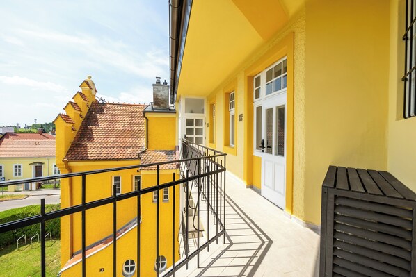 A yellow building with a balcony, a tiled roof, and a white door.