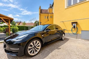 A black car parked in front of a yellow building with a charging station.