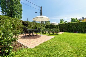 Un espace patio aménagé avec une table et des chaises, entouré d’une pelouse bien entretenue et d’une haie.