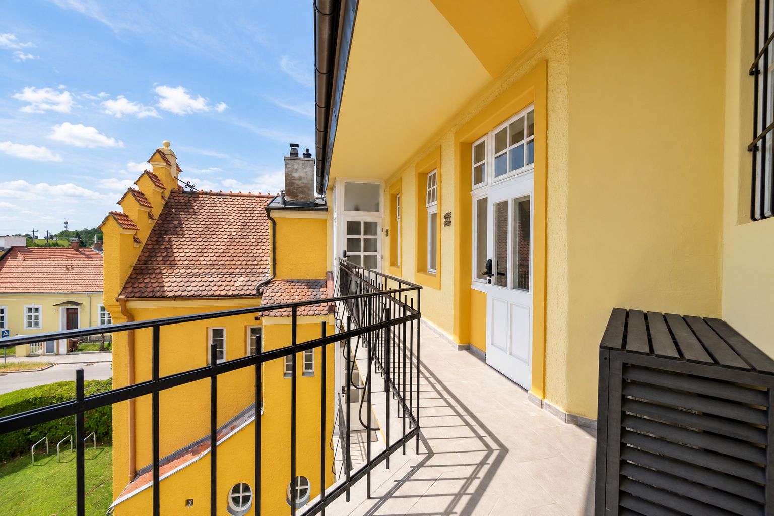 A yellow building with a balcony, a tiled roof, and a window with a white frame.