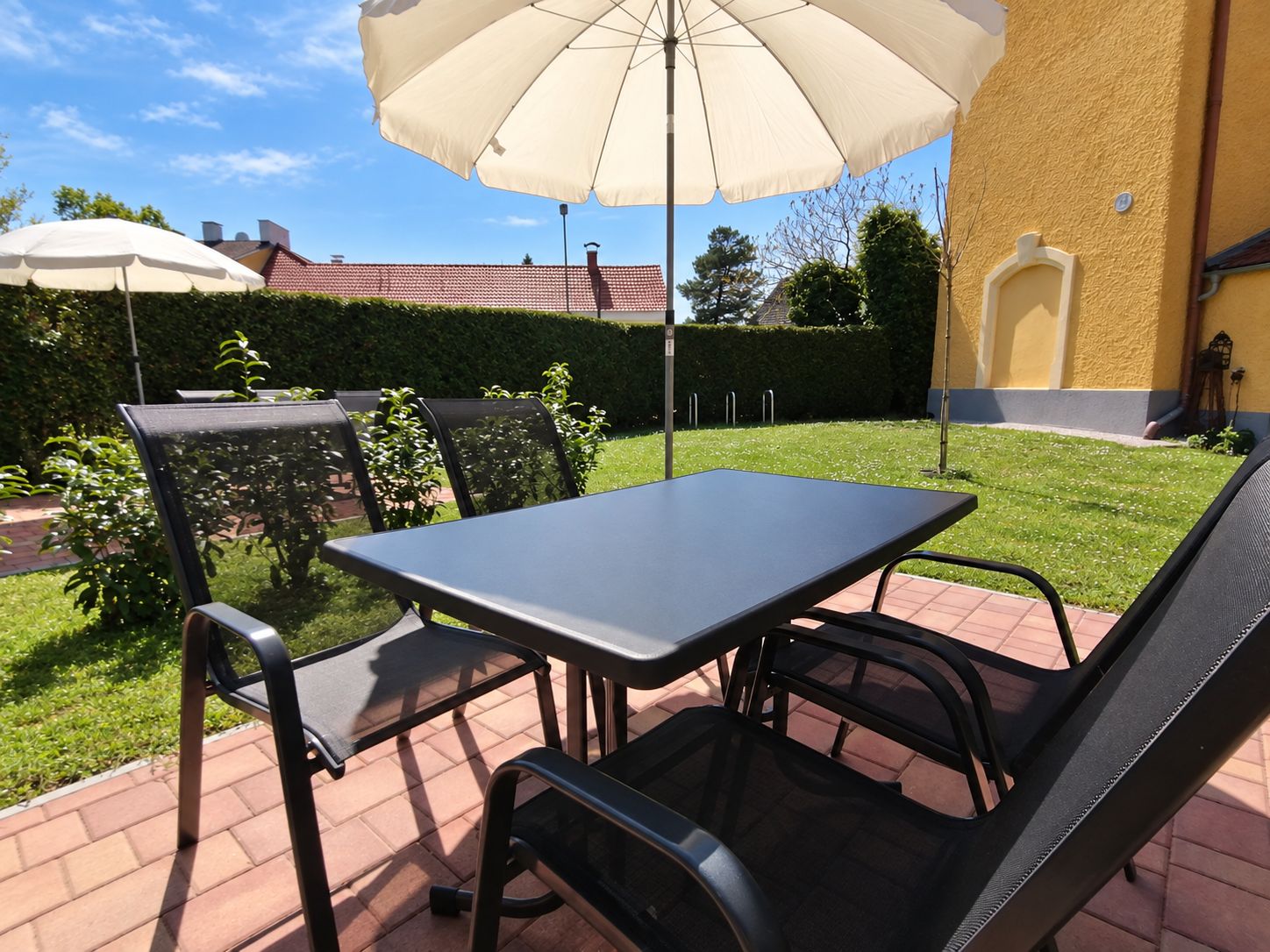 Eine Terrassengruppe im Freien mit Tisch, Stühlen und einem großen Sonnenschirm, eingebettet in einen gepflegten Rasen.