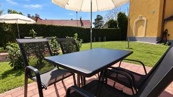 Eine Terrassengruppe im Freien mit Tisch, Stühlen und einem großen Sonnenschirm, eingebettet in einen gepflegten Rasen.