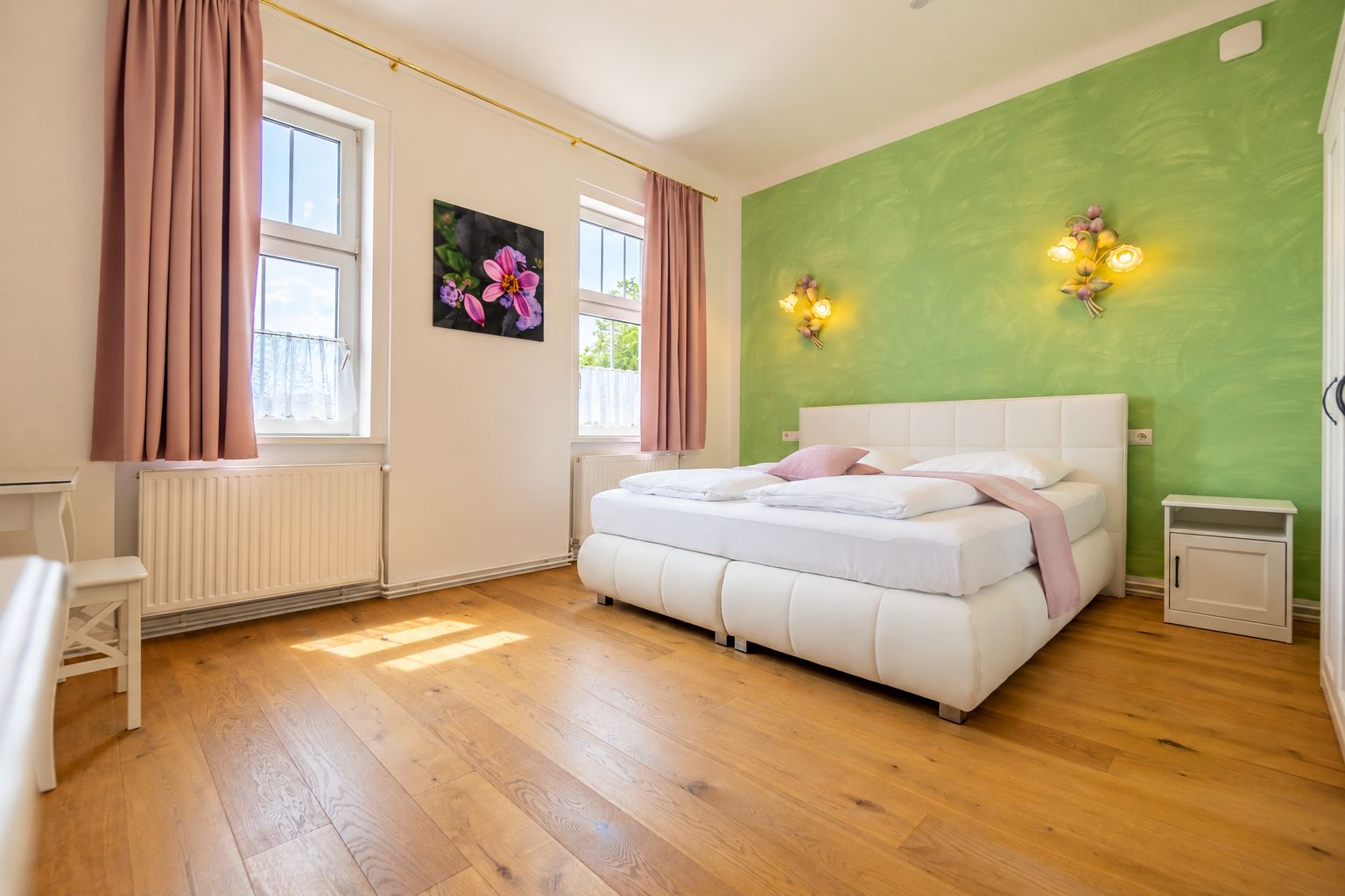 A bedroom with a white bed, a radiator, a desk, and a green wall.