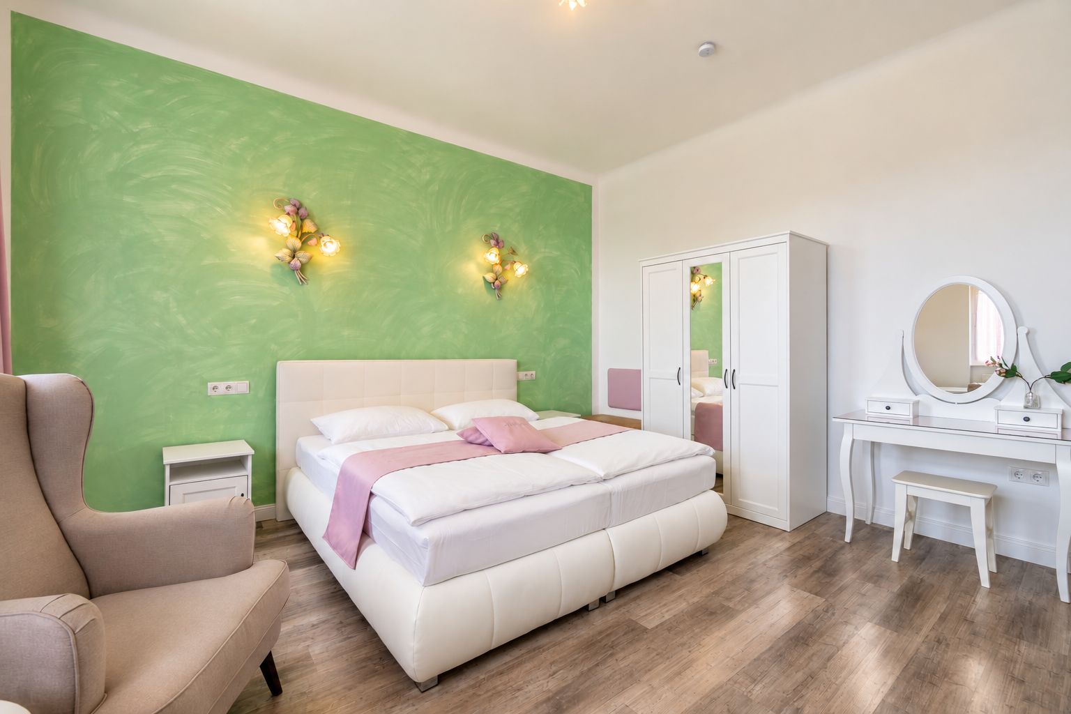 Een slaapkamer met een bed, nachtkastjes, een kaptafel met spiegel en een groene wand.